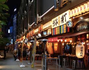 Una calle de noche con gente sentada en las mesas en Shibuya 渋谷 下北沢エリア 電動キックボードLUUP敷地内 駅徒歩3分 en Tokio