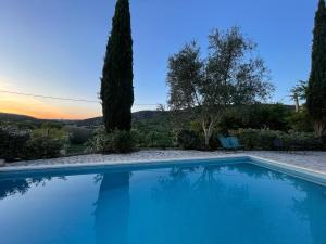 a blue swimming pool with a sunset in the background at Gîtes du Clos Cèze Art in Saint-André-de-Roquepertuis
