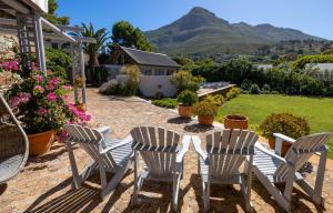 a patio with three chairs and a table with mountains in the background at Chapmans Peak Lodge Noordhoek Cape Town. in Cape Town