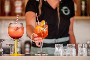 a woman is holding two cocktails in front of a bar at Beach Resort Agde in Le Grau-dʼAgde