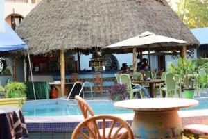 Lambada Holiday Resort Mombasa في متوابا: مطعم مع مسبح به طاولات وكراسي ومظلة