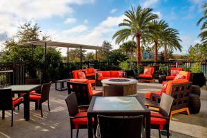 Courtyard by Marriott Orlando Lake Nona في أورلاندو: فناء في الهواء الطلق مع طاولات وكراسي وأشجار نخيل