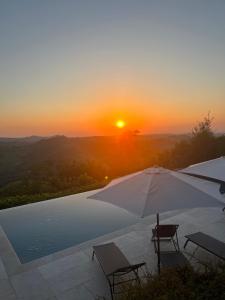 a pool with an umbrella and chairs and the sunset at Borgo dei Gatti Albergo Diffuso in Golferenzo