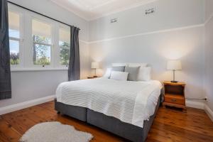 a white bedroom with a bed and two windows at Brightly Cottage in Mudgee