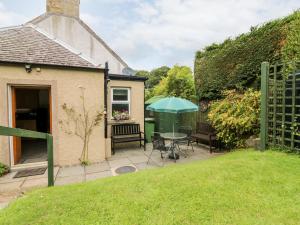 um pátio com uma mesa e um guarda-chuva verde em Katmoget Cottage em Cupar