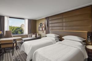 a hotel room with three beds and a window at Sheraton Grand Sydney Hyde Park in Sydney