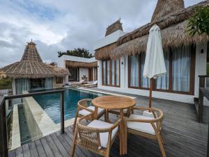 eine Holzterrasse mit Tisch und Stühlen neben einem Swimmingpool in der Unterkunft Umarato Villa Sumba in Rua