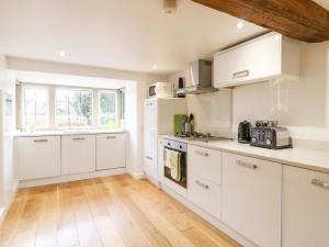 a kitchen with white cabinets and a wooden floor at Fern Cottage in Bakewell