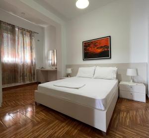 a white bedroom with a large white bed and wooden floors at Port Side Sarande in Sarandë