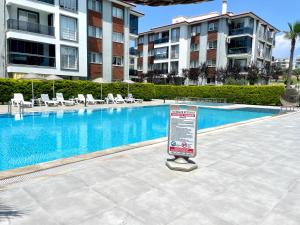 a sign in front of a swimming pool with buildings at Theos Holiday Apartments Room 23 Family Suit Accommodation For Families Only in Kuşadası