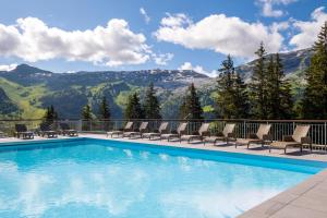 a swimming pool with chairs and mountains in the background at Résidence Pierre & Vacances Premium Les Terrasses d'Eos in Flaine +80 photos