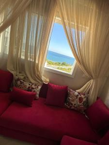 um sofá vermelho em frente a uma janela com o oceano em Immeuble Familial Imad em Tetouan