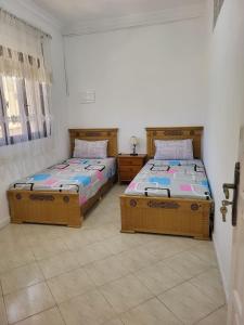two twin beds in a room with two windows at Appartement Tanger 2 in Tangier