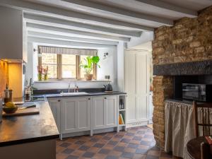 a kitchen with white cabinets and a stone wall at Armada Cottage in Charlbury +17 photos