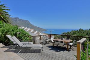 una terraza de madera con mesa, sillas y el océano en Camps Bay Villa Views Pool Garden, en Ciudad del Cabo