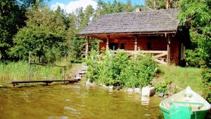 een hut op een rivier met een boot ervoor bij Lakefront Log House and Sauna in Ginučiai