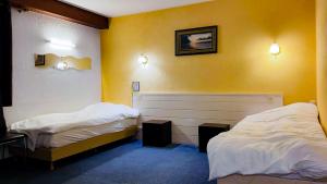 - 2 lits dans une chambre aux murs jaunes dans l'établissement Hôtel Le Valéran, à Ligny-en-Barrois