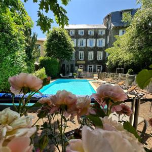 a swimming pool with pink flowers in front of a building at Logis Le Relais de Fusies in Lacaune