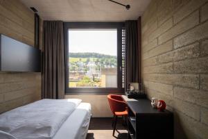 um quarto com uma cama, uma secretária e uma janela em Tailormade Hotel LEO St Gallen em St. Gallen