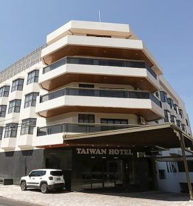 ein weißes Auto, das vor einem hohen Gebäude parkt in der Unterkunft Taiwan Hotel in Ribeirão Preto