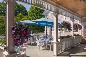 een patio met tafels en blauwe parasols en paarse bloemen bij Old Stagecoach Inn in Waterbury