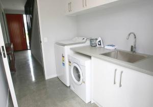 uma cozinha branca com um lavatório e uma máquina de lavar roupa em Glenvue em Lake Tekapo