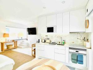 a white kitchen with white cabinets and a living room at Casa de Praia - Almograve in Almograve