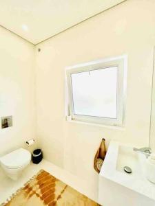 a white bathroom with a toilet and a window at Casa de Praia - Almograve in Almograve