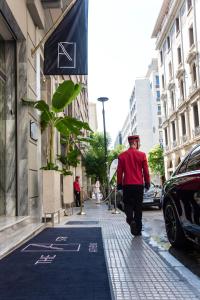 Un homme en chemise rouge et chapeau marchant dans une rue dans l'établissement Athens The L7 Str - Luxury Boutique Collection Hotel, à Athènes