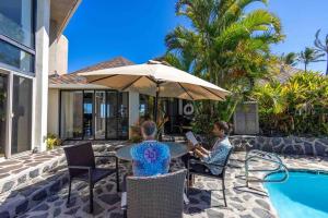 twee mensen aan een tafel met een parasol naast een zwembad bij Opulent Waterfall House with Ocean Views in Haiku, Maui in Huelo