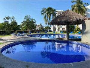 a large swimming pool with a straw umbrella and chairs at Departamento nuevo a estrenar! in Manzanillo