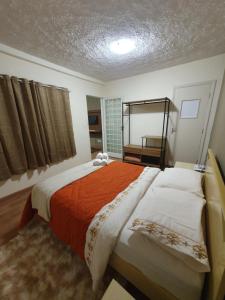 um quarto com 2 camas com lençóis laranja e branco em Villa Ida Acomodações, 3 suítes aconchegantes e charmosas no centro em Serra Negra