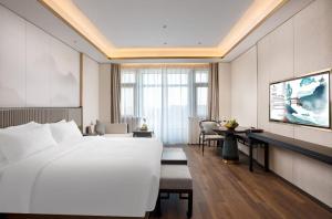 Hangzhou Junsun Luxury Hotel في هانغتشو: غرفة في الفندق مع سرير أبيض كبير ومكتب