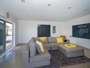 Aquila Waters - Whitianga Holiday Home في وايتيانغا: غرفة معيشة مع أريكة رمادية ووسائد صفراء