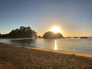 a beach with the sun setting on the water at Graydon Grove in Kaiteriteri