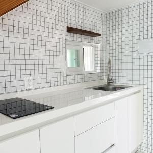 La salle de bains est pourvue de carrelage blanc, d'un lavabo et d'un miroir. dans l'établissement Rooftop Moonlight Pension, à Gangneung