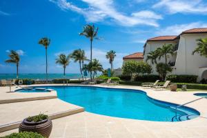 a swimming pool with palm trees and the ocean at Beach Living at Villas Pappagallo Beachfront 22 in West Bay