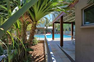 a swimming pool with palm trees and a building at Woodgate Beach Houses in Woodgate