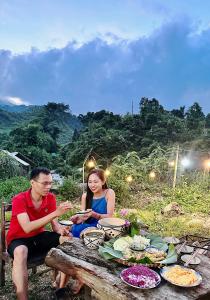 a man and woman sitting at a picnic table with food at Lũng Mười Homestay in Nà Giảo