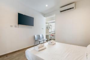 a white bedroom with a bed and a flat screen tv at Studio 32 - Apartment & kitchenette at the new Olo living in Paceville