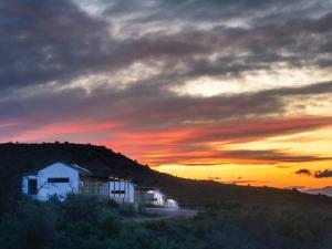 a building on a hill with a sunset in the background at Klein Doorn Farm Stay in Oudtshoorn