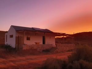 a house in the desert with the sunset in the background at Klein Doorn Farm Stay in Oudtshoorn