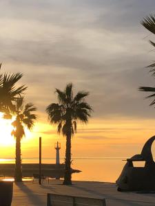 une plage avec des palmiers et un phare au coucher du soleil dans l'établissement Gîte du centre- Maison avec extérieur en centre ville, à Mèze