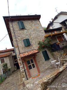 una casa de piedra con persianas verdes y una puerta en B&B La Rocchetta dal Sròz, en Le Serucce