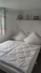 Una cama blanca con dos almohadas encima. en MOBILHEIM HERZ LAUWERSOOG - Chalet Robbengat, en Lauwersoog