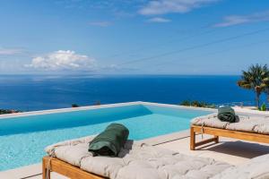 a swimming pool with two beds and the ocean at Premium villa panoramic sea-view Calheta Pearl in Estreito da Calheta