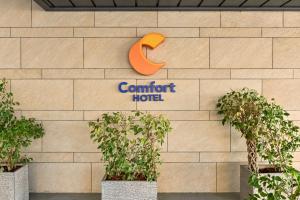a sign for a comfort hotel on a wall with trees at Comfort Hotel Jeddah King Road in Jeddah