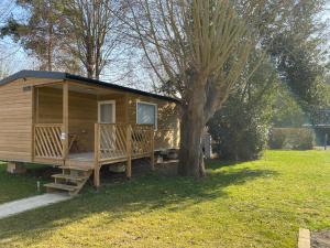 a wooden cabin with a porch next to a tree at Paris Camping Ile du Roi in Triel-sur-Seine