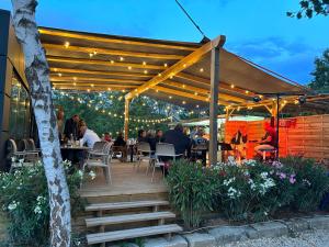 Una terraza de madera con gente sentada en mesas bajo una pérgola. en Paris Camping Ile du Roi, en Triel-sur-Seine