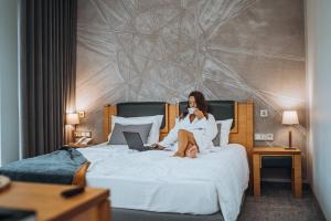 Eine Frau sitzt mit einem Laptop auf einem Bett. in der Unterkunft Gabija Hotel SPA & Conferences in Palanga